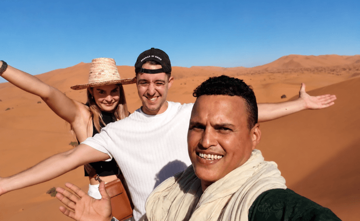 Tourists and guide taking a selfie together among the golden dunes of Erg Chebbi desert in Morocco